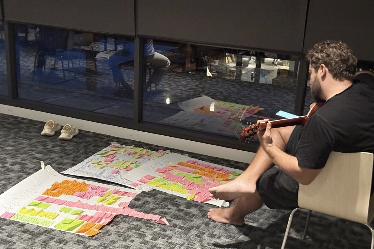 A participant sitting barefoot with a guitar beside a floor of sticky-note sheets, rethinking a life plan