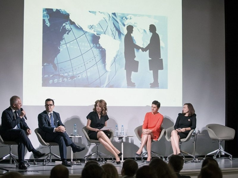A panel discussion on stage, five speakers in armchairs